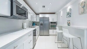 A modern kitchen with stainless steel appliances, white cabinetry, and a bar area with white stools. - Beautiful Vacation Rental Directly on beach (Hollywood)