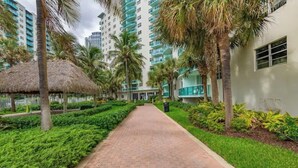 A pathway lined with palm trees and a thatched-roof structure, leading to a building with balconies. - Beautiful Vacation Rental Directly on beach (Hollywood)