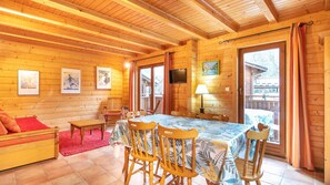 A wooden cabin interior with a dining table, chairs, a sofa, and a TV mounted on the wall. - Cosy chalet 4/6 ppl with balcony (Morillon)