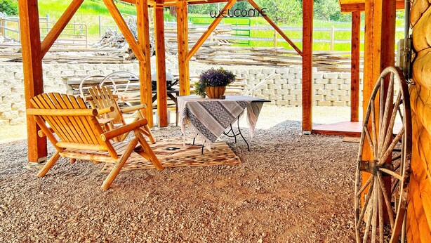 Une structure rustique en bois, avec une table et des chaises, un luminaire suspendu et une grande roue.