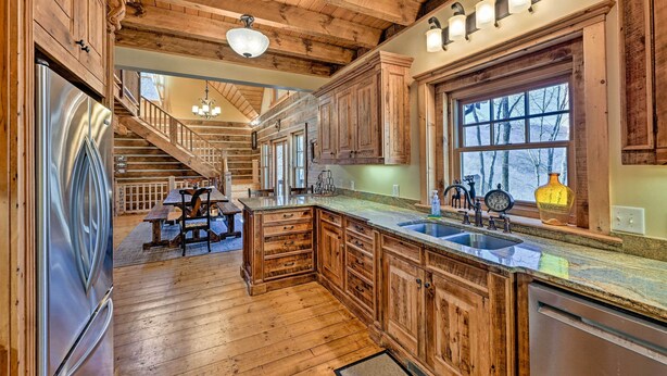 A wooden kitchen with a large island, stainless steel appliances, and a window with a view of trees. - Hot Tub & Fire Pit: Getaway Near Nantahala Gorge! (Franklin)