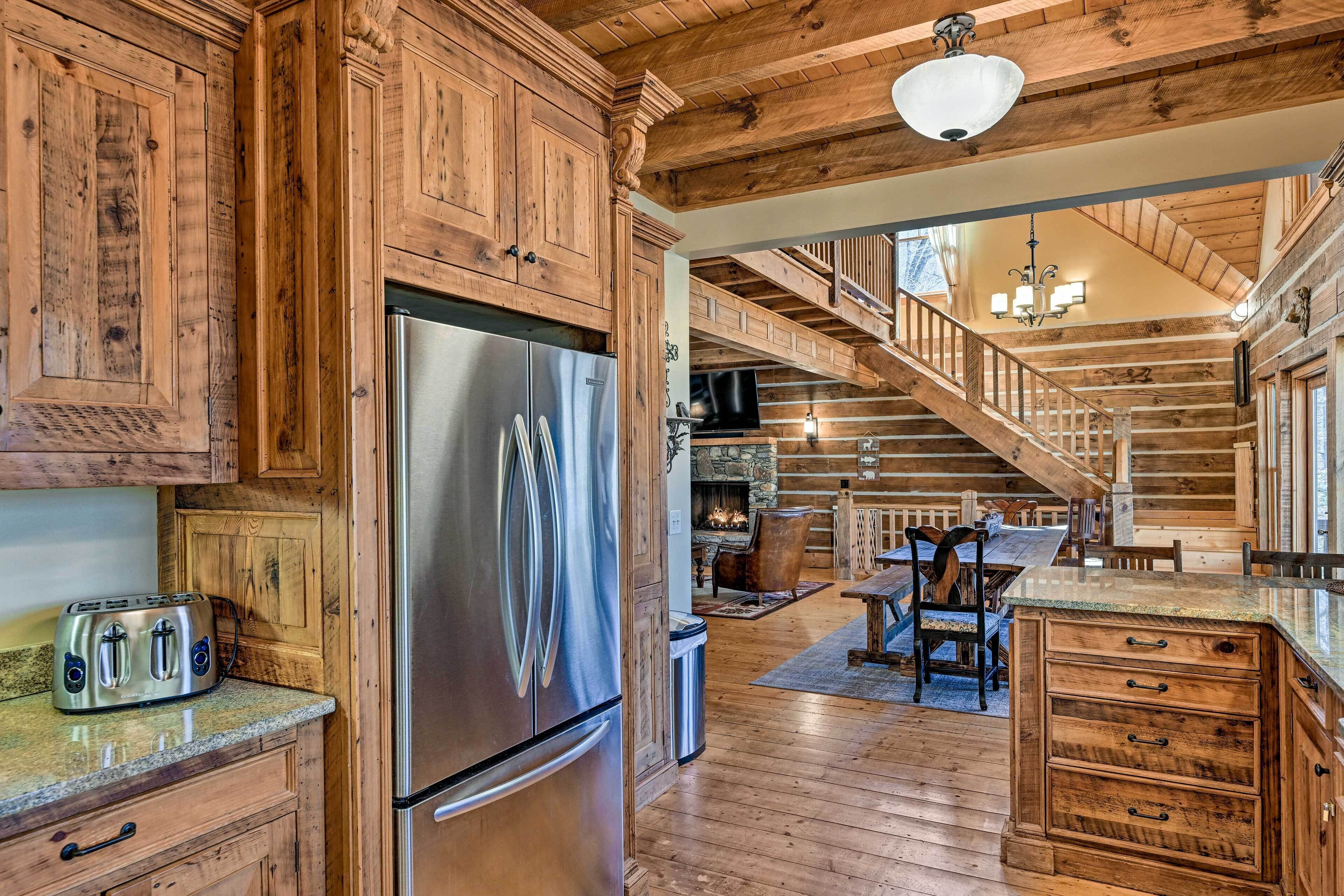 A rustic kitchen with wooden cabinets, a stainless steel refrigerator, and a stone fireplace.
