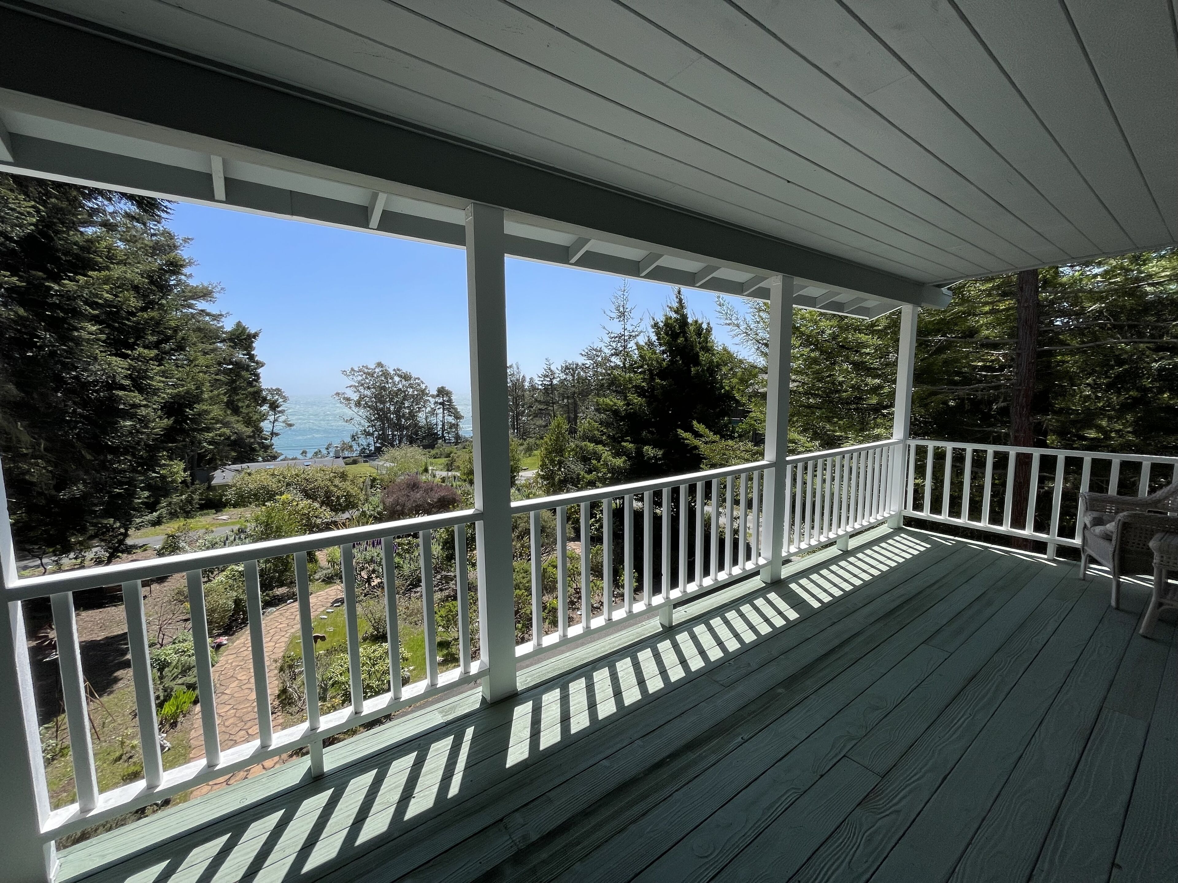 A covered porch with a view of a landscaped garden and a body of water.