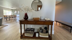 Une console en bois, surmontée d’un miroir, avec un vase de fleurs blanches et deux paniers tressés posés sur le sol.