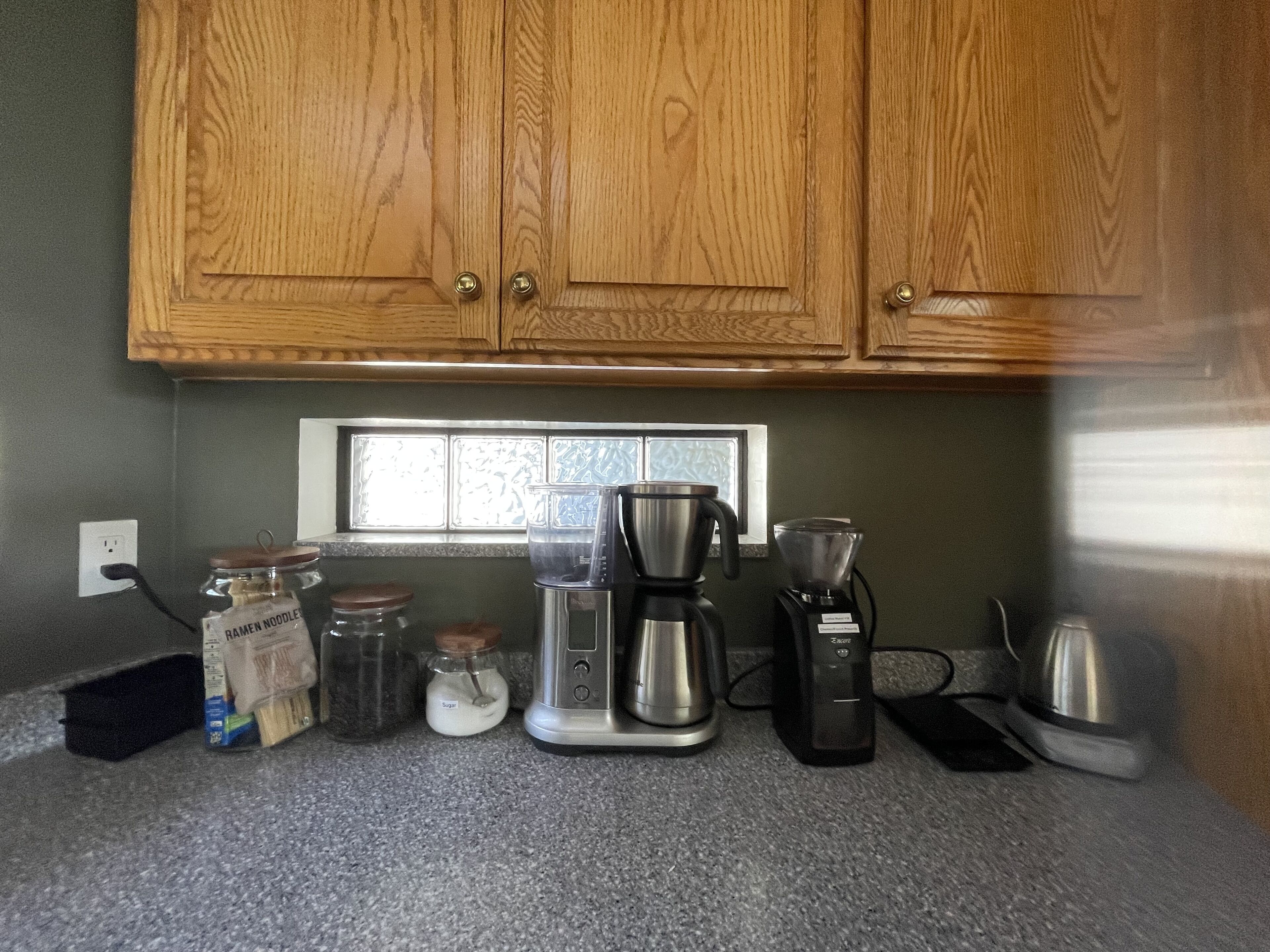 Una cocina con armarios de madera, un ventanal y varios electrodomésticos, incluyendo una cafetera y una licuadora.