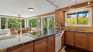 A modern kitchen with a large island, wooden cabinets, and large windows offering a view of greenery.