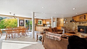 A spacious living area with a fireplace, a dining area with wooden chairs, and a kitchen in the background.