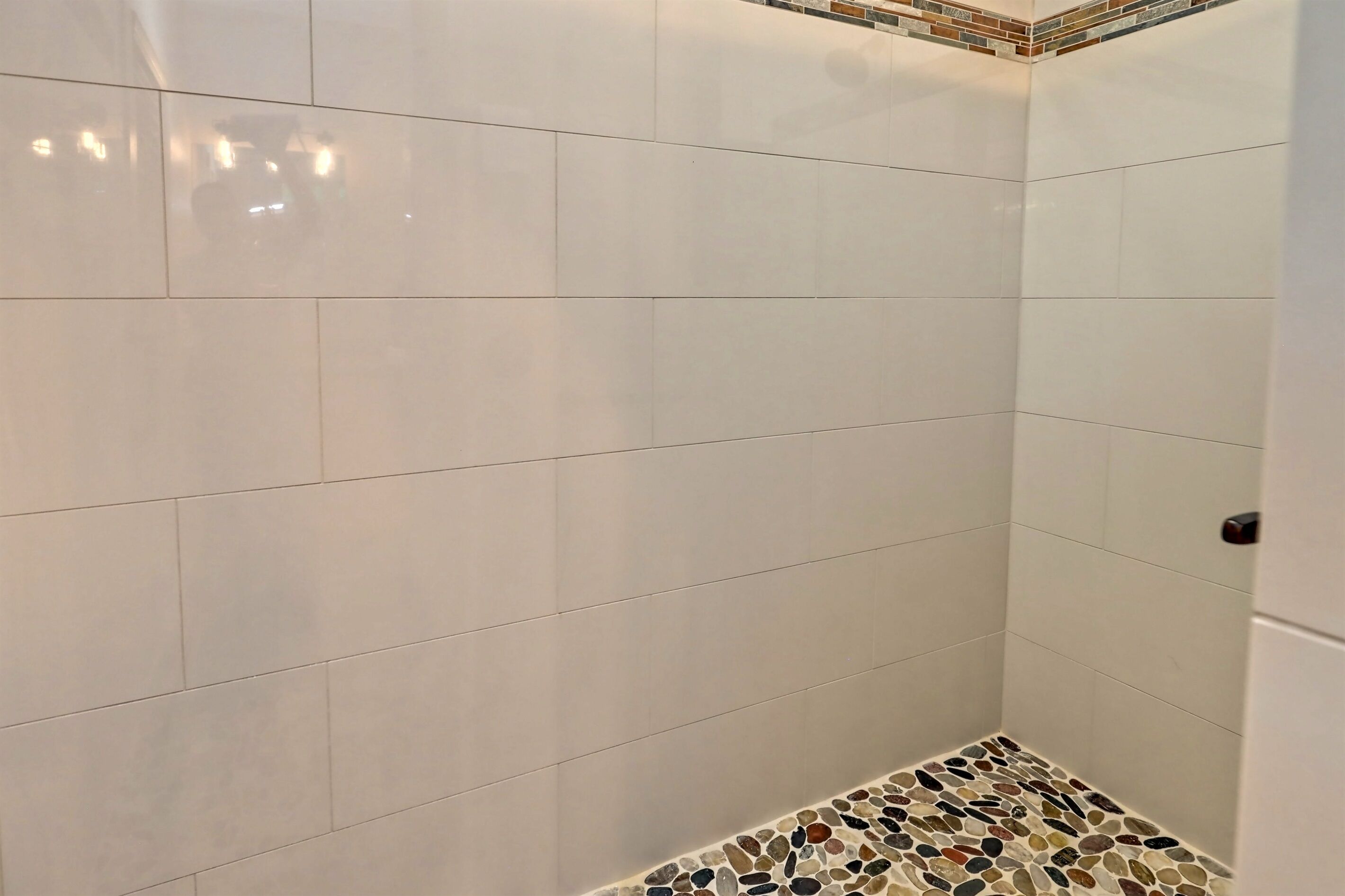 A bathroom with white tiles and a mosaic tile border at the bottom.