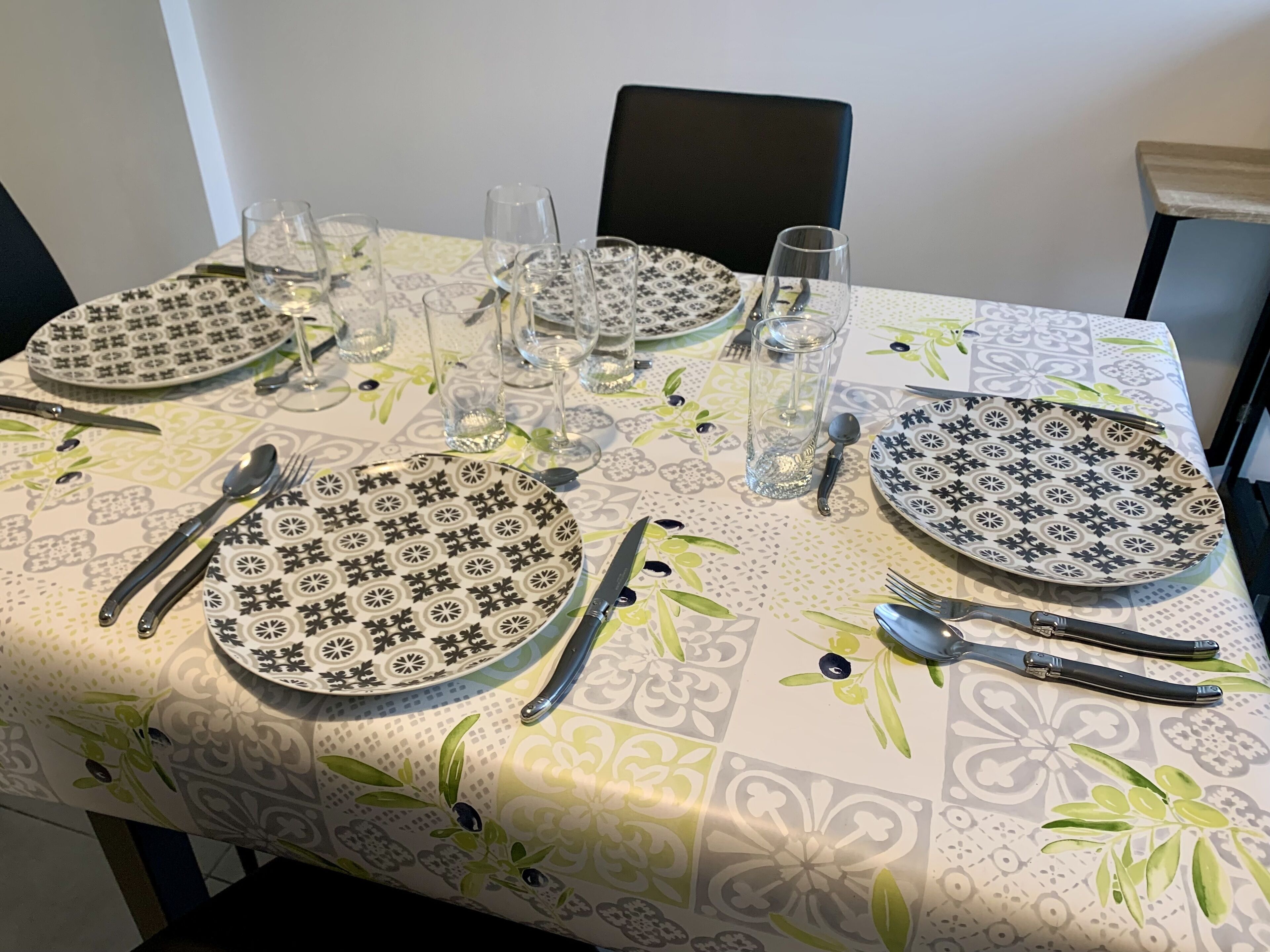 A dining table set with plates, cutlery, and glasses, covered with a patterned tablecloth.