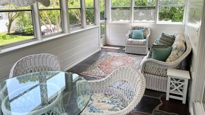 Une véranda meublée de meubles en osier, dotée de grandes fenêtres et d’une table en verre.