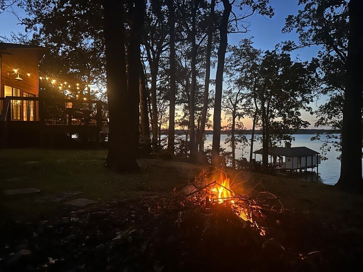 Un chalet au bord du lac, doté d’un foyer extérieur, entouré d’arbres et agrémenté d’un quai.
