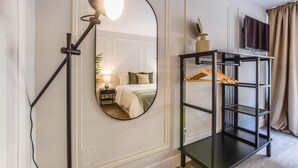 A hotel room with a bed, a mirror, a TV, and a black shelving unit with a hanging rack. - Spectacular design apartment in the center SB 1 (Madrid)