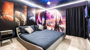 Une chambre avec un grand lit, une table de chevet et une fresque murale représentant des scènes spatiales.