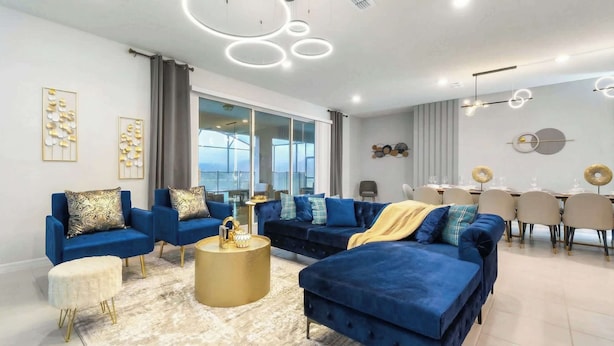 A modern living room with a blue sofa set, a gold coffee table, and a dining area with a white table and chairs.
