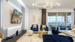 Un salon moderne avec un téléviseur, des canapés bleus, une table basse ronde dorée et un balcon avec un barbecue.