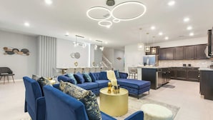 A modern living room with a sectional sofa, a dining area, and a kitchen with dark cabinetry.
