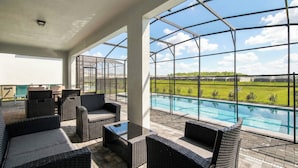 A covered outdoor area with wicker furniture, a pool, and a view of a green landscape.