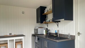 Uma cozinha compacta com armários escuros, bancada branca e micro-ondas embutido. Há banquetas de madeira e uma pequena prateleira sobre a pia.