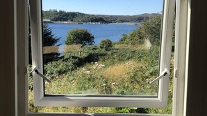 Janela com vista para um lago, árvores e colinas.
