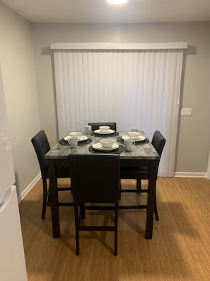 Comedor con una mesa dispuesta para cuatro personas, rodeada de sillas, con persianas verticales de fondo.