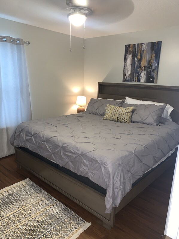 Un dormitorio con cama, mesita de noche, lámpara, ventilador de techo y un cuadro en la pared.