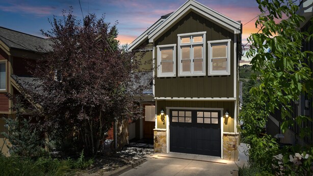 Une maison à deux étages, avec une façade d’un vert foncé, un garage avec une porte noire et une entrée bien éclairée.