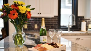Un plan de travail de cuisine orné d’un vase en verre rempli de fleurs, d’une bouteille de vin et d’une planche à fromages avec divers fromages et olives.