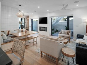 Un salon moderne avec une table à manger en bois, un canapé et un fauteuil, une cheminée et un téléviseur fixé au mur.