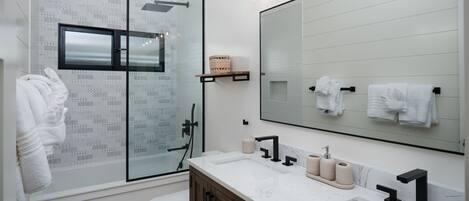 Uma casa de banho moderna com chuveiro envidraçado, um espelho grande e um lavatório branco com bancada de mármore.