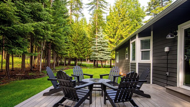 A deck with a table and chairs, surrounded by a lawn and trees. - Perfectly located home between ski resort and downtown Whitefish- AC for hot days (Whitefish)