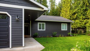 A residential house with a dark exterior, a front door, a covered porch, and a well-maintained lawn with small shrubs and flowers. - Perfectly located home between ski resort and downtown Whitefish- AC for hot days (Whitefish)