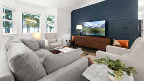 A modern living room with a grey sofa, a wooden cabinet, and a TV on the wall. - Perfectly located home between ski resort and downtown Whitefish- AC for hot days (Whitefish)