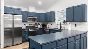 A modern kitchen with blue cabinets, stainless steel appliances, and a large island. - Perfectly located home between ski resort and downtown Whitefish- AC for hot days (Whitefish)
