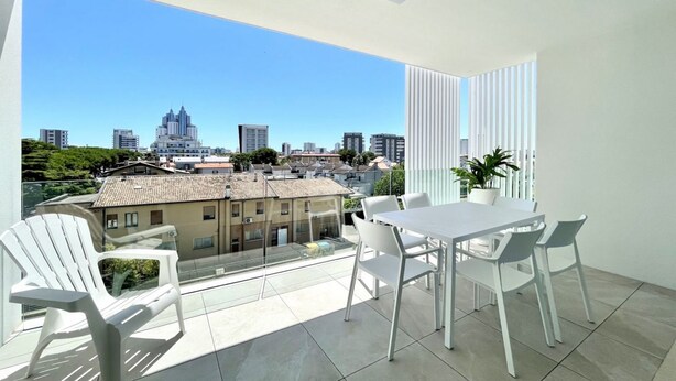 A balcony with a table and chairs, a potted plant, and a city view.
