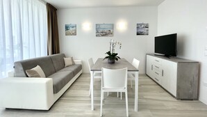 A modern living room with a sofa, dining table, chairs, a TV, and artwork on the wall.