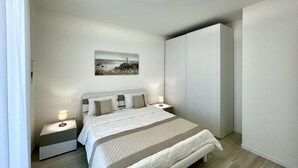 A modern bedroom with a bed, bedside tables, a nightstand, a wardrobe, and a ceiling light fixture.