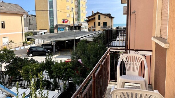 Un balcón con vista a una calle, un coche estacionado y un edificio con una bandera.
