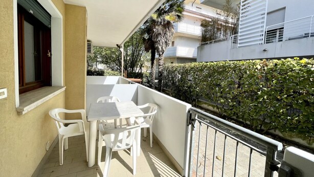 A balcony with a table and chairs, a window with a shutter, and a hedge.