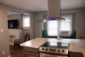 A kitchen with a central island, a stove, and a large window with blinds. - Convenient Cozy Home - Dog & Family Friendly (Akron)