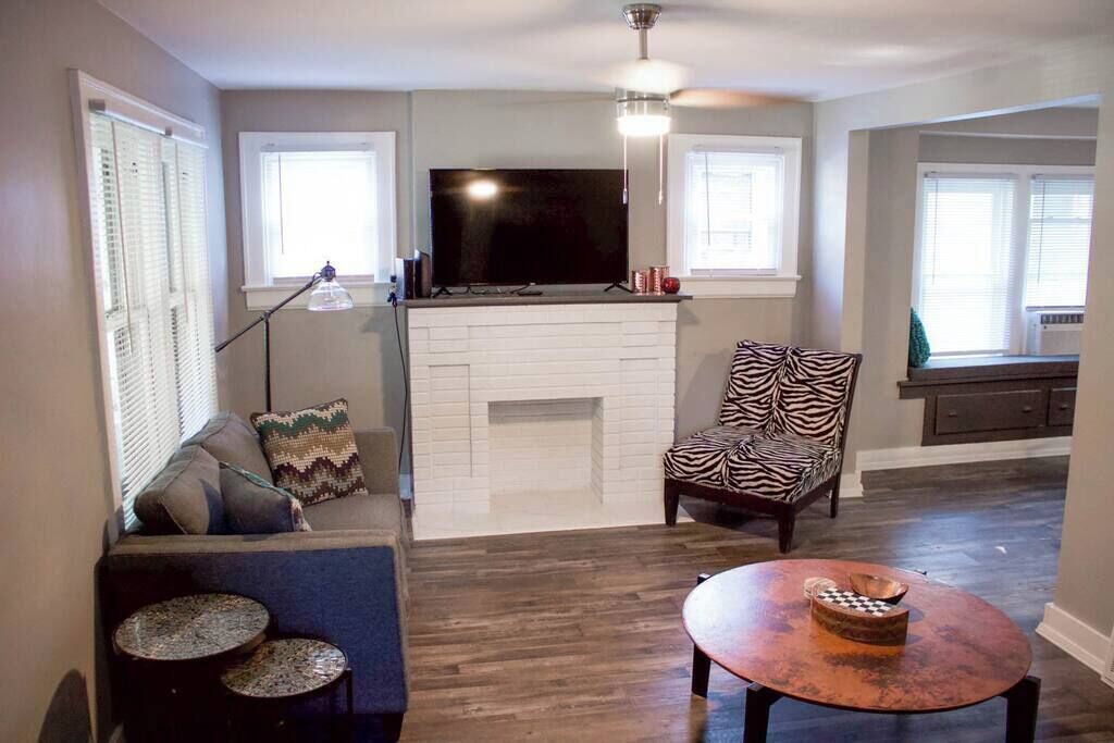 A living room with a fireplace, a television, a zebra-patterned chair, and a round table with a bowl.