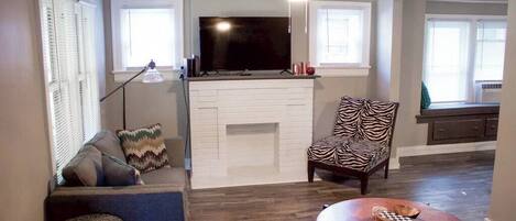 A living room with a fireplace, a television, a zebra-patterned chair, and a round table with a bowl.