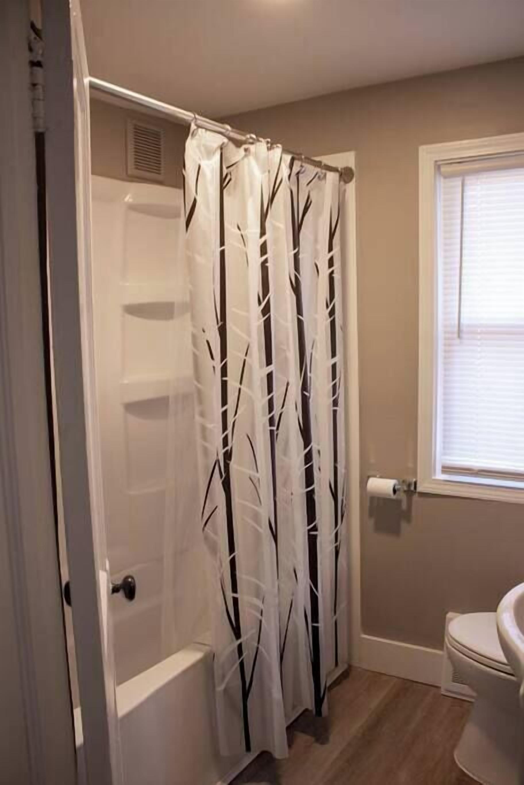 A bathroom with a shower curtain, a toilet, and a window.