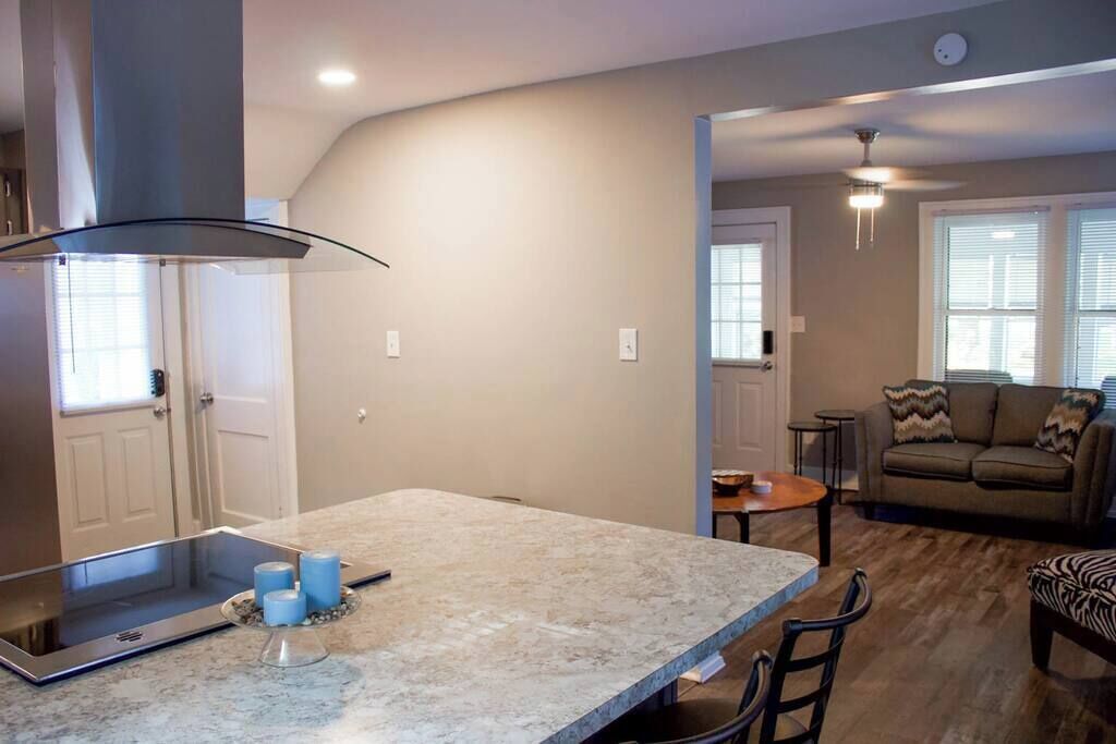 Una cocina moderna con una isla grande, un comedor con mesa y sillas, y una sala de estar con sofá y televisor.