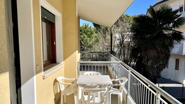Un balcon avec une table et des chaises, une fenêtre avec un store et une rambarde.
