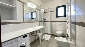 Une salle de bain moderne avec une douche à parois de verre, un lave-linge encastré, un lavabo et des toilettes.