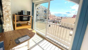 Uma varanda com vista para edifícios, uma mesa de madeira com um cardápio e um micro-ondas em uma prateleira.