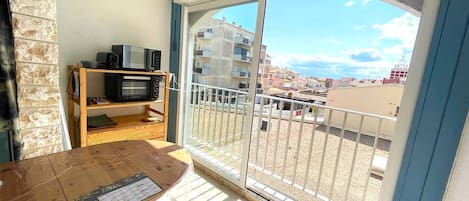 A balcony with a view of buildings, a wooden table with a menu, and a microwave on a shelf.