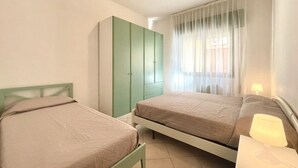 Un dormitorio con dos camas, un armario verde y una ventana con cortinas.