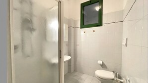 Un baño pequeño y limpio con inodoro, lavamanos y cabina de ducha.