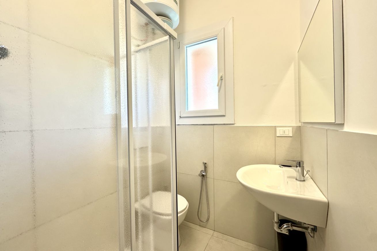 A bathroom with a glass shower enclosure, a toilet, and a sink.